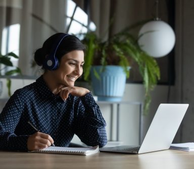 Happy young indian girl with headphones looking at laptop screen.